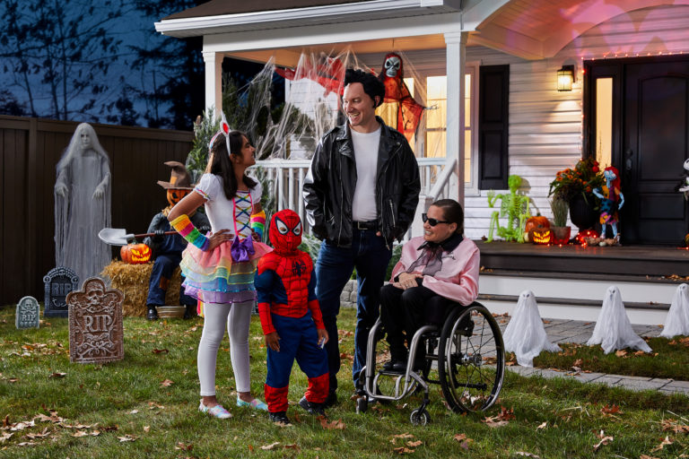 A family wearing halloween costumes in front of a house decorated with spiderwebs and tombstones.
