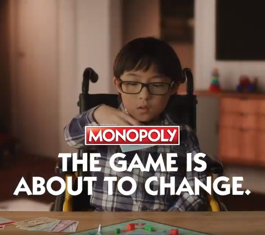 A kid sits on a wheel chair and is playing Monopoly game.